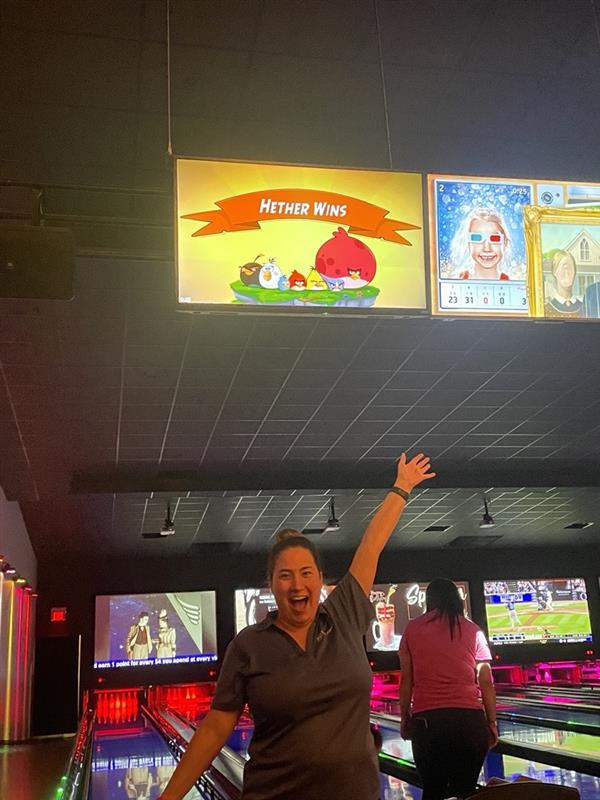 Woman celebrates bowling win under scoreboard.