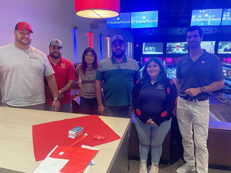Group poses by a table with red cloth in bowling alley.