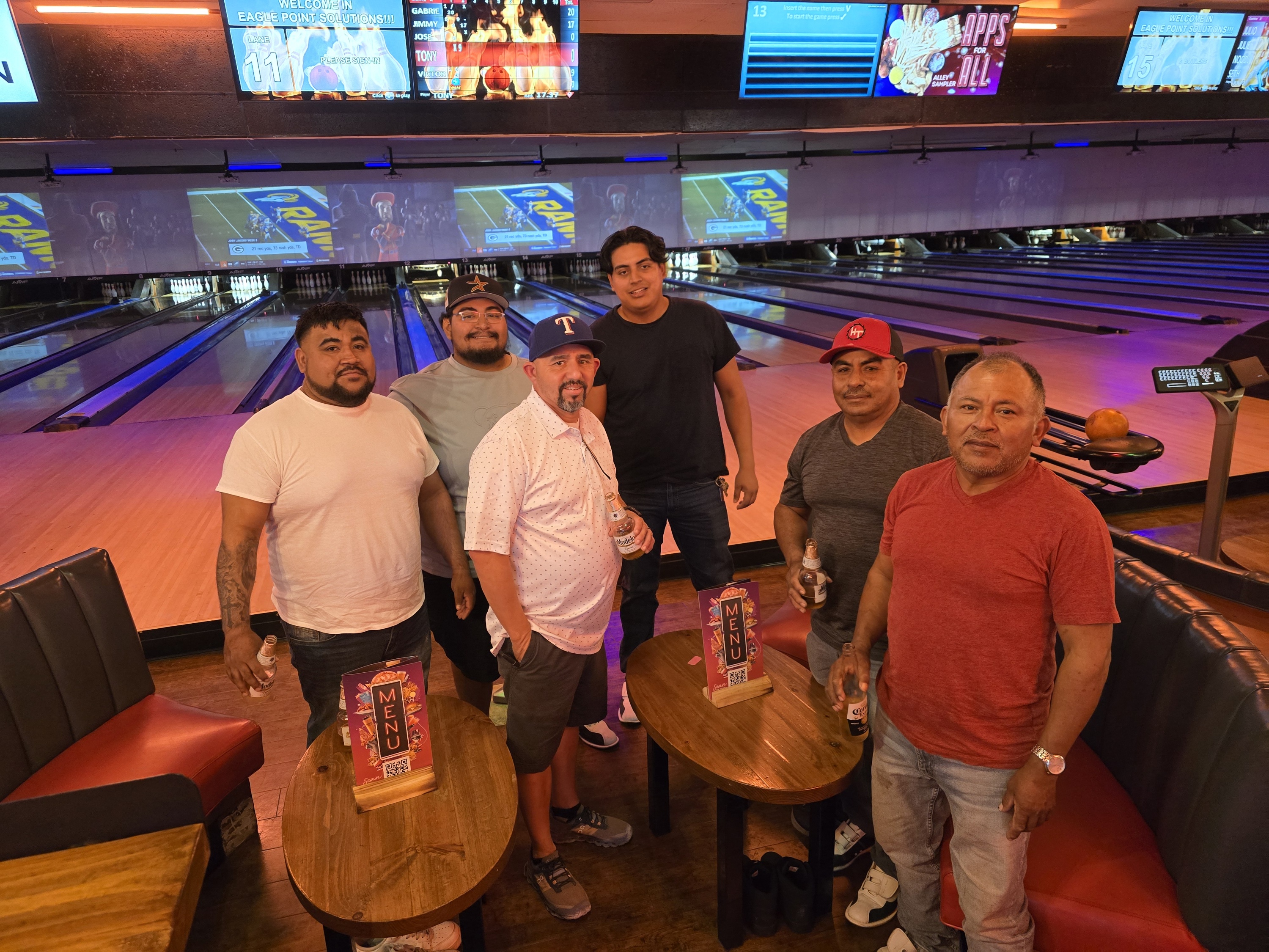 Group of men posing by a bowling lane with drinks.