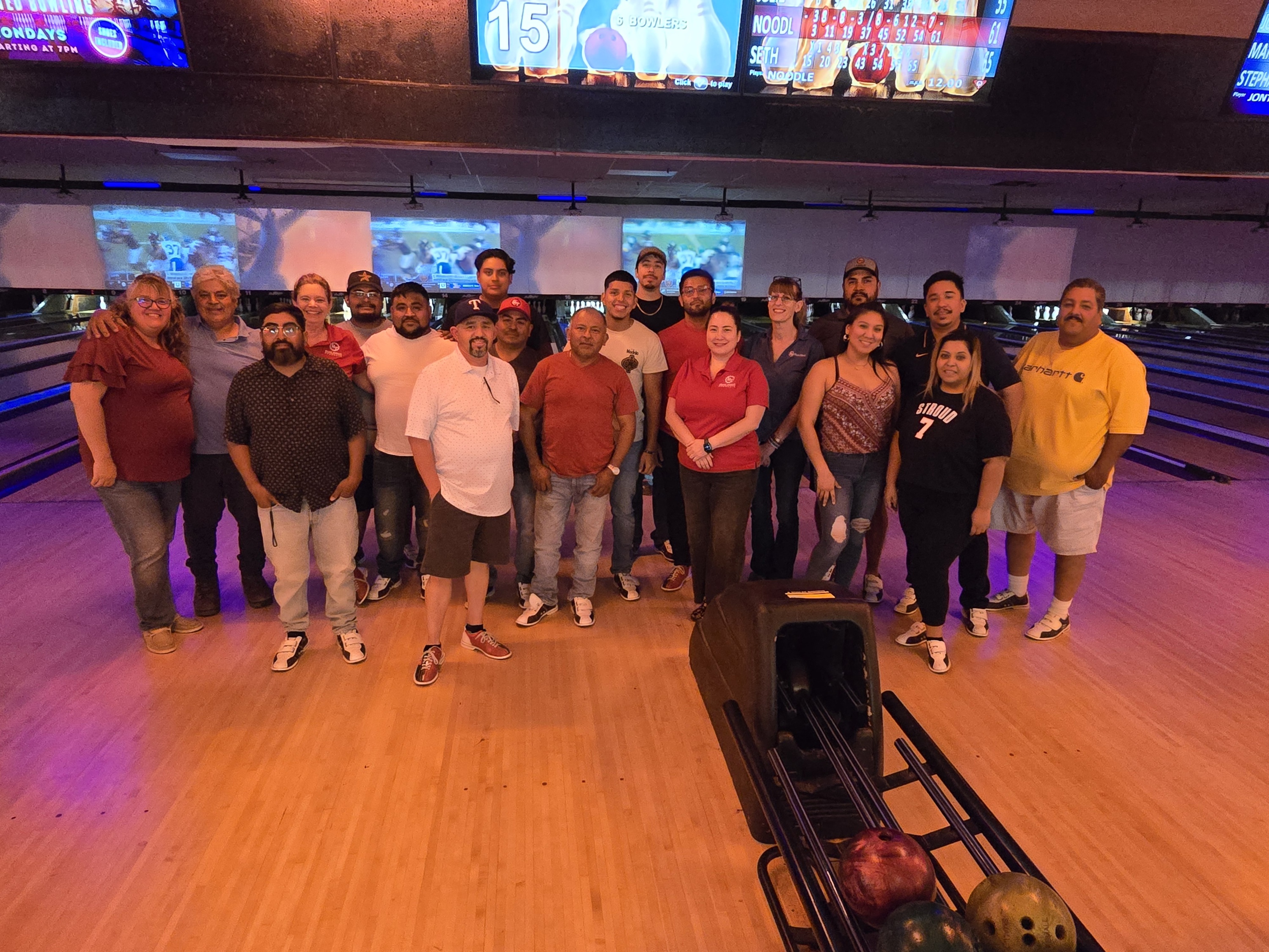 Large group poses in bowling alley, lanes visible.