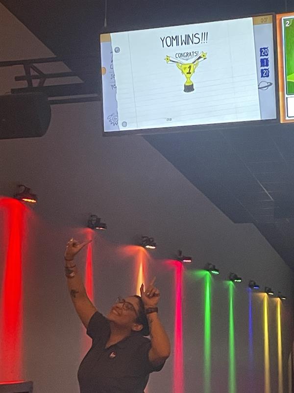 Woman celebrates bowling victory under scoreboard.